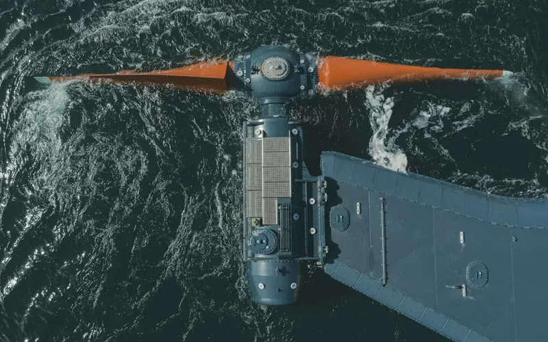 Orbital turbine, t-shaped with large orange blades at the front in the dark ocean offshore of Orkney