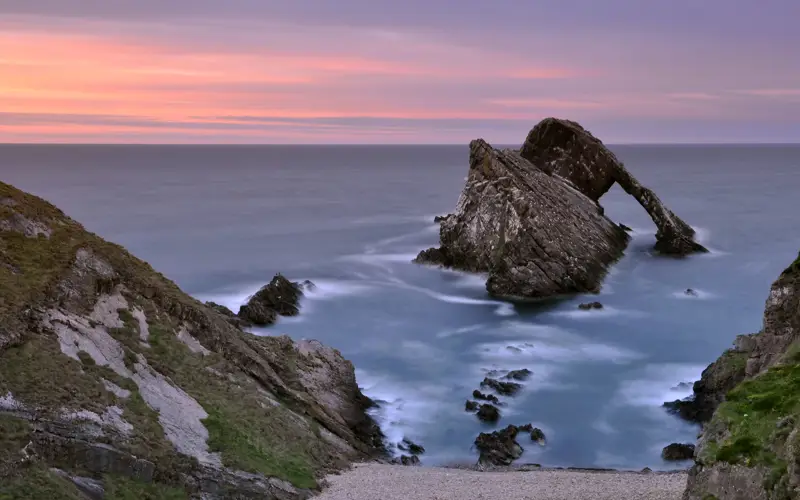 Bow Fiddle Rock in Moray sitting against purple and pink sunset over the sea