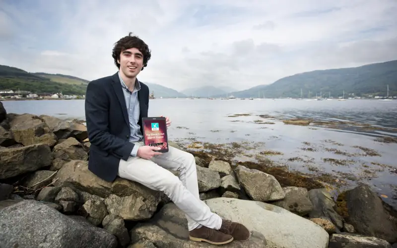 Sam Coley from technology company SAMTEQ sits on stoney shoreline holding award trophy award