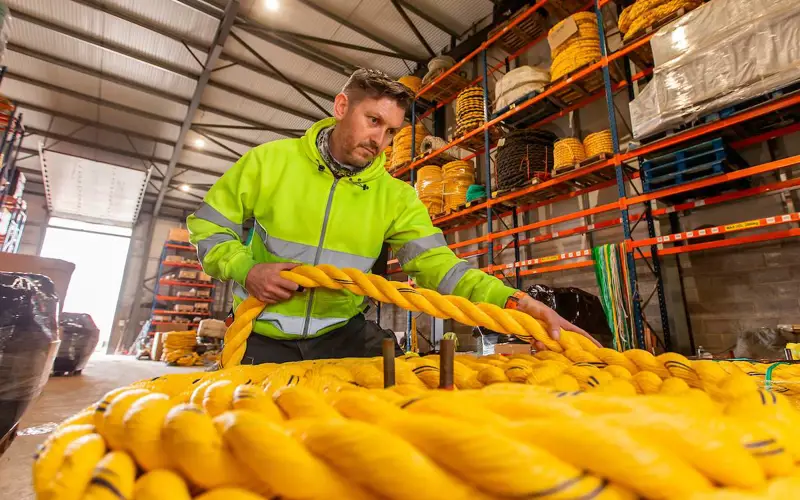 Employee at Gael Force group working with bright yellow, thick ropes wearing high vis yellow jacket