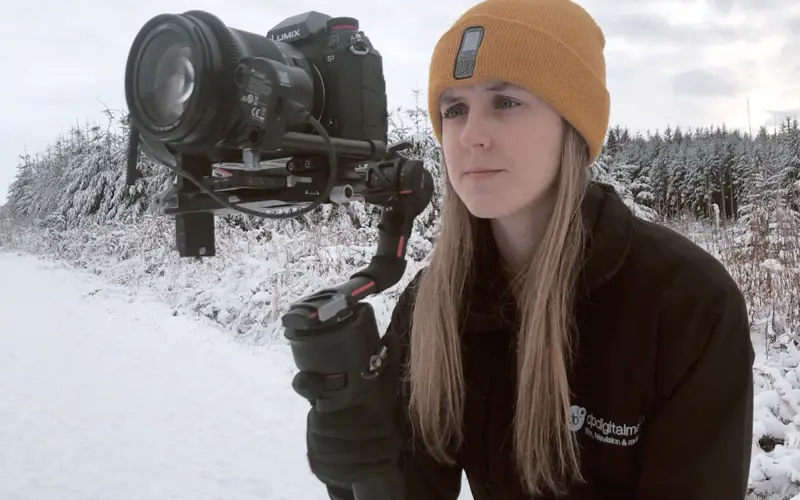 Woman holding handheld camera against a snowy backdrop 